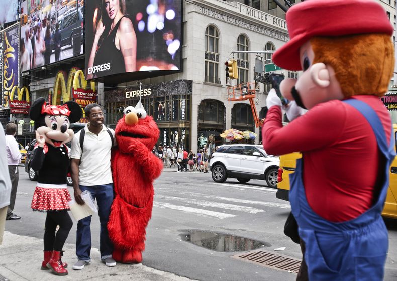 Un visitante de Times Square posa para un retrato con personas disfrazadas de personajes famosos el lunes 28 de julio de 2014 en Nueva York. El alcalde de Nueva York Mayor Bill de Blasio dijo el lunes que considera que la gente que trabaja disfrazada en T