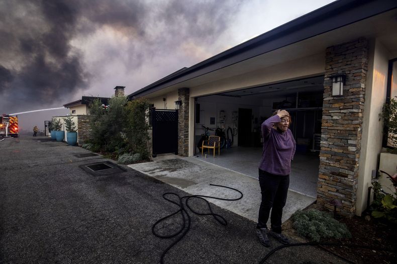 Una vecina se ve de pie delante de un garaje mientras los bomberos combaten el incendio de Palisades, en el vecindario de Pacific Palisades en Los Ángeles, el martes 7 de enero de 2025. (AP Foto/Ethan Swope)