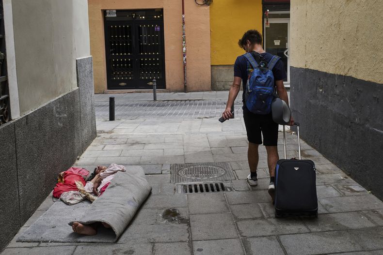 Un turista camina junto a una persona sin hogar en el centro de Madrid, España, el martes 3 de junio de 2025. (AP Foto/Bernat Armangue)