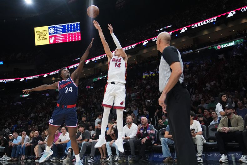 Tyler Herro (14), del Heat de Miami, dispara un triple mientras Kobe Brown (24), de los Clippers de Los Ángeles, defiende durante la primera mitad del juego de baloncesto de la NBA, el lunes 1 de diciembre de 2025, en Miami. (AP Foto/Lynne Sladky)