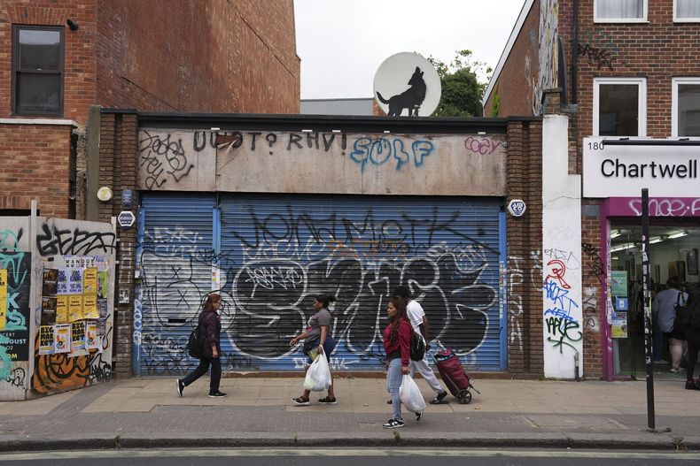 Personas caminan pasa junto a una nueva obra de arte que representa un lobo aullando creada por Banksy sobre una antena parabólica colocada en el techo de una tienda en Peckham, al sur de Londres, el jueves 8 de agosto de 2024. (Jordan Pettitt/PA via AP)