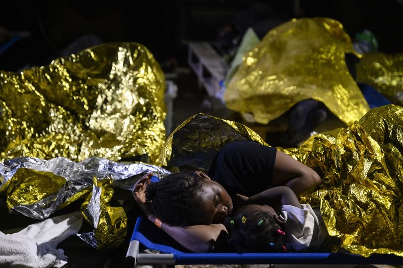 Una mujer y una niña duermen ante el centro de recepción de migrantes en Lampedusa, Sicilia, la mañana del jueves 14 de septiembre de 2023. El centro de recepción de la isla sureña de Lampedusa, en Italia, seguía en una situación crítica el jueves mientras trataba de gestionar la llegada de miles de migrantes que desembarcaron en un margen de 24 horas esta semana. (AP Foto/Valeria Ferraro)