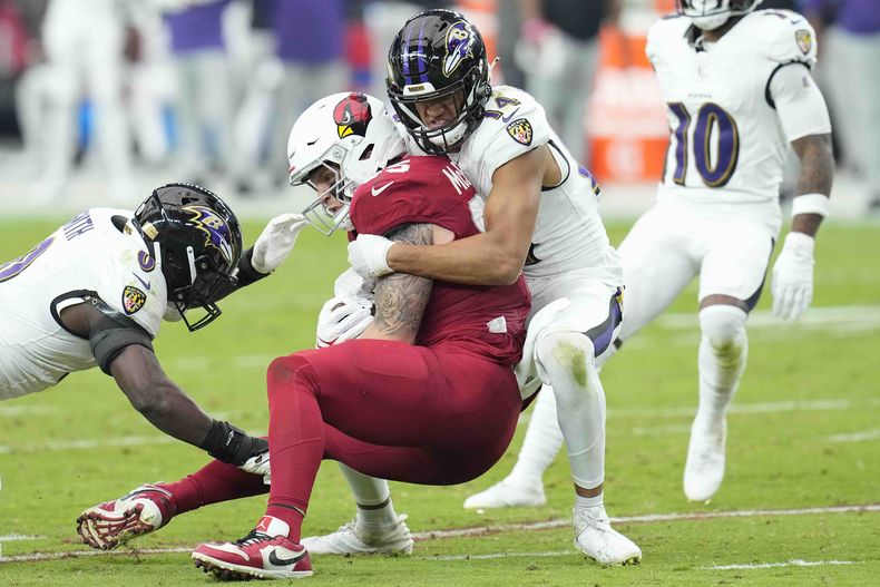 El tight end de los Cardinals de Arizona Trey McBride (centro) es detenido por el safety de los Ravens de Baltimore Kyle Hamilton (derecha) durante la segunda mitad del juego del domingo 29 de octubre de 2023, en Glendale, Arizona. (AP Foto/Ross D. Franklin)