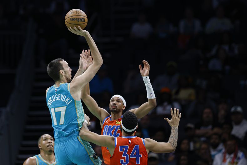 El alero de los Hornets de Charlotte, Aleksej Pokusevski (17), dispara sobre los escoltas del Thunder de Oklahoma City, Aaron Wiggins, centro, y Kenrich Williams (34) durante la segunda mitad de un partido de baloncesto de la NBA en Charlotte, Carolina del Norte, el domingo 7 de abril de 2024. (AP Foto/Nell Redmond)