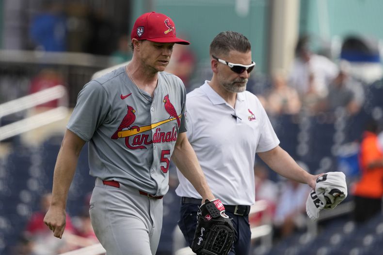 Sonny Gray, izquierda, abridor de los Cardenales de San Luis, camina acompañado por el trainer Adam Olsen después de abandonar el juego en la segunda entrada del juego de preparación contra los Nacionales de Washington, el lunes 4 de marzo de 2024, en West Palm Beach, Florida. El equipo anunció que Gray tiene rigidez en el tendón de la corva derecho. (AP Foto/Jeff Roberson)