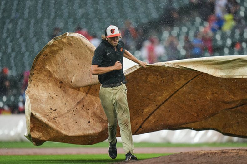 Un miembro del equipo de protección del campo de juego coloca una lona sobre el montículo para protegerlo de la lluvia durante un partido de béisbol de Grandes Ligas entre los Orioles de Baltimore y los Filis de Filadeflia que fue postergado por el clima, el domingo 2 de agosto de 2026, en Baltimore. (AP Foto/Stephanie Scarbrough)