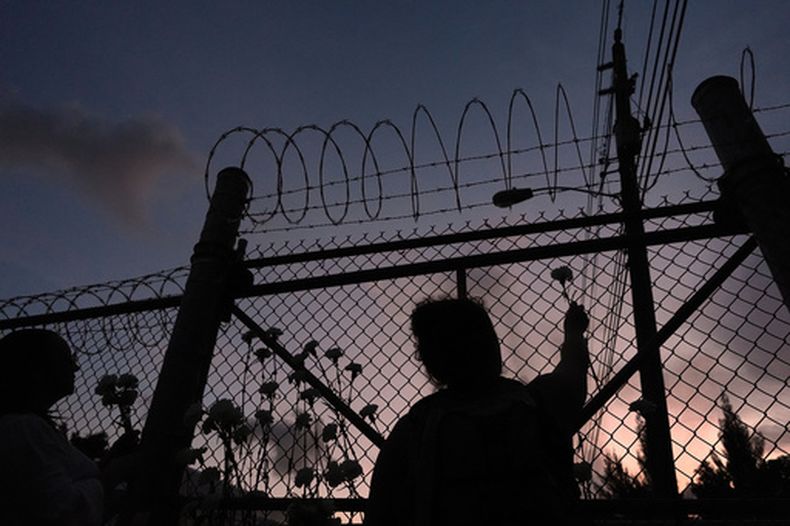 ARCHIVO – Varias personas observan las flores en una cerca fuera del Centro de Detención Krome en Miami, el sábado 24 de mayo de 2025, durante una vigilia para homenajear a las personas que han muerto bajo custodia del Servicio de Inmigración y Control de Aduanas (ICE, por sus siglas en inglés) y a quienes han resultado afectados por las deportaciones masivas. (AP Foto/Rebecca Blackwell, Archivo)