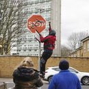Una persona retira una obra de arte de Banksy que parece mostrar tres drones sobre un cartel de Stop que fue develado en la intersección de las calles Southampton Way y Commercial Way en Peckham, sureste de Londres, viernes 22 de diciembre de 2023. (Aaron Chown/PA via AP)
