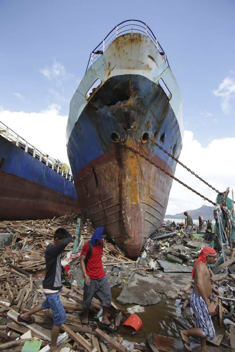 Sobrevivientes pasan cerca de un buque de gran calado que fue arrastrado a tierra por el oleaje provocado por el devastador tif&oacute;n Haiyan en la ciudad de Tacloban, capital de la provincia de Leyte, en el centro de Filipinas el domingo 10 de noviembr