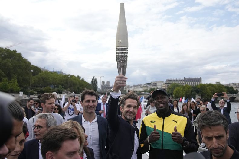 El diseñador francés Mathieu Lehanneur alza la antorcha de los Juegos Olímpicos de París 2024 junto a Usain Bolt, el martes 25 de julio de 2023, en París. (AP Foto/Christophe Ena)