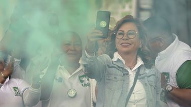 La candidata presidencial Sandra Torres, del partido UNE, sostiene un teléfono celular en medio de humo verde al cerrar su campaña en el mercado La Terminal en Ciudad de Guatemala, el viernes 18 de agosto de 2023. (AP Foto/Moisés Castillo)