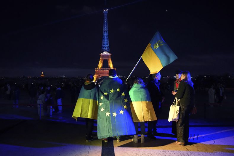 ARCHIVO – Un grupo de ucranianos sostienen banderas de Ucrania y la Unión Europea mientras la torre Eiffel es iluminada con los colores de Ucrania para conmemorar el tercer aniversario de la invasión rusa a ese país, en París, el 24 de febrero de 2025. (AP Foto/Christophe Ena, Archivo)