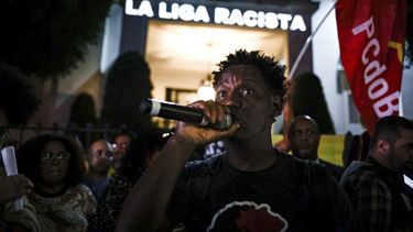Delante de un mensaje proyectado en la fachada del consulado de España en Sao Paulo, un manifestante habla durante una protesta contra las expresiones racistas lanzadas a Vinícius Júnior, el martes 23 de mayo de 2023 (AP Foto/Tuane Fernandes)