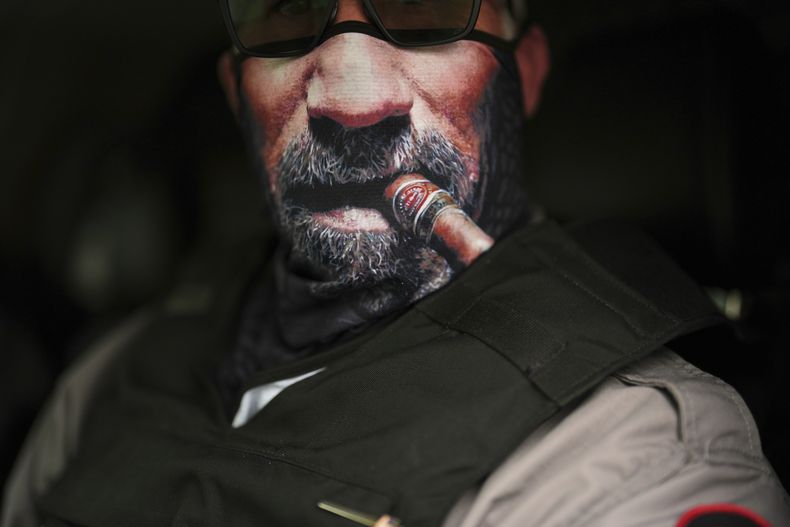 Un agente de inmigración se cubre el rostro con una mascarilla con la imagen de un habano y barba mientras espera a trasladar a inmigrantes detenidos, el miércoles 23 de julio de 2025, en Baldwin Park, California. (AP Foto/Gregory Bull)