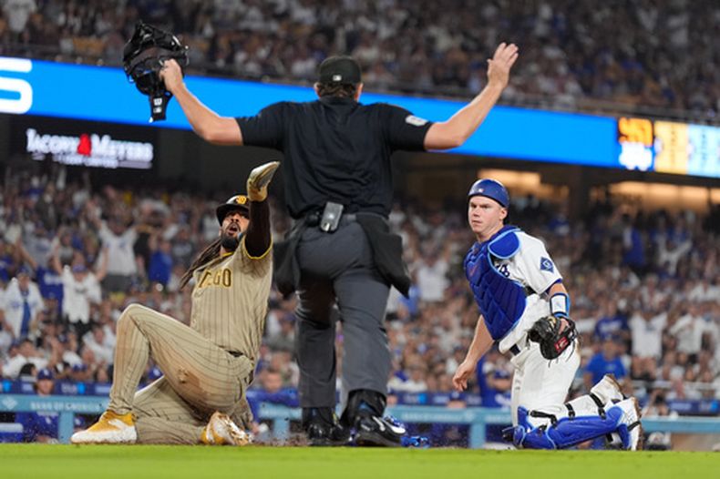 Fernando Tatis Jr., izquierda, observa la decisión del umpire después de anotar con un elevado de sacrificio de Manny Machado después de que el receptor de los Dodgers de Los Ángeles, Will Smith, no lo pudiera retirar en la quinta entrada del juego de béisbol de Grandes Ligas, el miércoles 23 de septiembre de 2026, en Los Ángeles. (AP Foto/Mark J. Terrill)