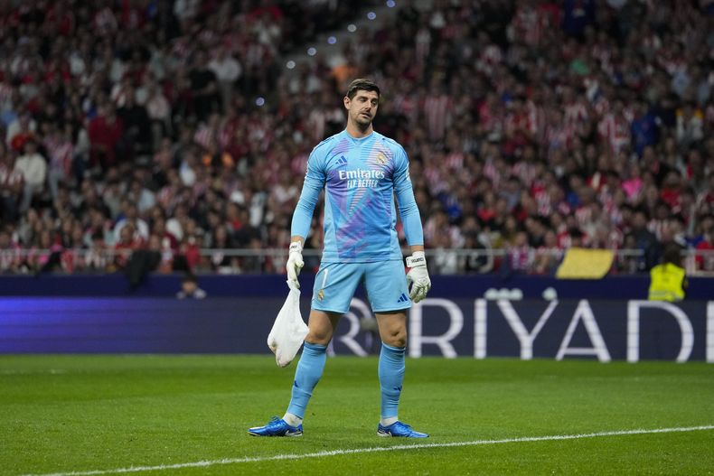 El arquero del Real Madrid Thibaut Courtois carga una bolsa arrojada por hinchas del Atlético de Madrid durante el partido contra Real Madrid, el domingo 29 de septiembre de 2024. (AP Foto/Bernat Armangue)