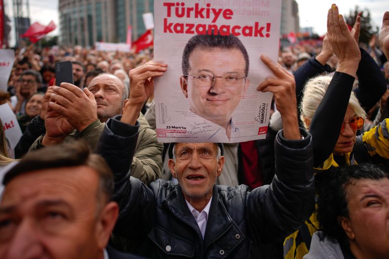 Gente coreando lemas durante una marcha en apoyo del encarcelado alcalde de Estambul, Ekrem Imamoglu, que comparecía para una vista en la corte de Caglayan, en Estambul, Turquía, el domingo 26 de octubre de 2025. El cartel con la imagen de Imamoglu dice en turco: Turquía ganará. (AP Foto/Emrah Gurel)
