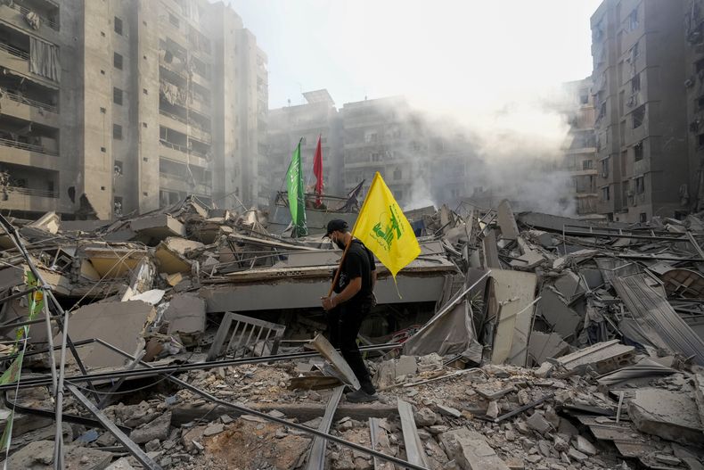 Un hombre carga una bandera de Hezbollah mientras camina sobre los escombros de su apartamento en Dahiyeh, en Beirut, Líbano, que fue destruido por un bombardeo de Israel el viernes 1 de noviembre de 2024. (AP Foto/Hassan Ammar)