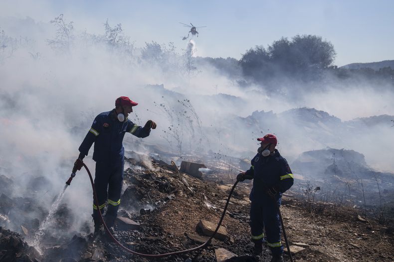 Los bomberos intentan extinguir el fuego mientras un helicóptero hidrante deja caer agua en el suburbio de Koropi, al este de Atenas, el miércoles 19 de junio de 2024. (AP Fotos/Petros Giannakouris)