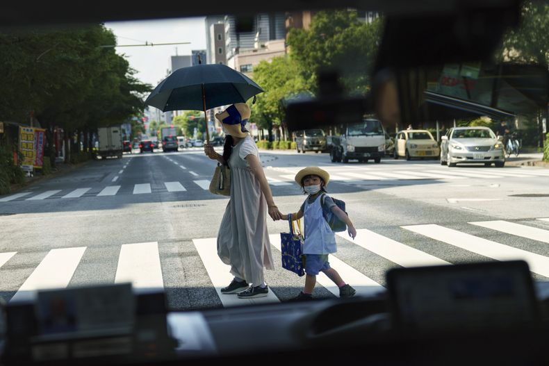 ARCHIVO - Una peatona que cruza una calle con una niña es retratada a través de la ventanilla de un taxi en Tokio, el lunes 19 de julio de 2021. (AP Foto/David Goldman, Archivo)