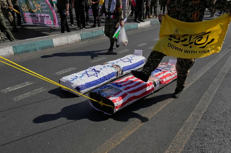 Un miembro de la Guardia Revolucionaria de Irán pisa ataúdes simulados cubiertos con banderas israelíes y estadounidenses mientras sostiene una pancarta que dice Abajo los EEUU durante un desfile de estilo militar organizado por el Estado en Teherán, Irán, el viernes 18 de septiembre de 2026. (AP Foto/Vahid Salemi)