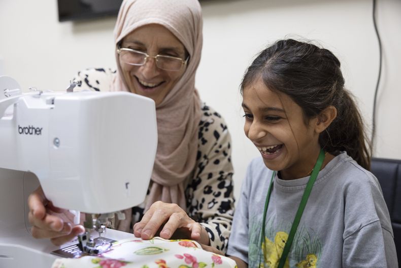 Amal Alalim ayuda a un estudiante en una clase de costura en Olive Community Services, el martes 29 de julio de 2025, en Fullerton, California. La clase fue parte del Campamento de Verano Intergeneracional de la organización. (AP Foto/Zoë Meyers)