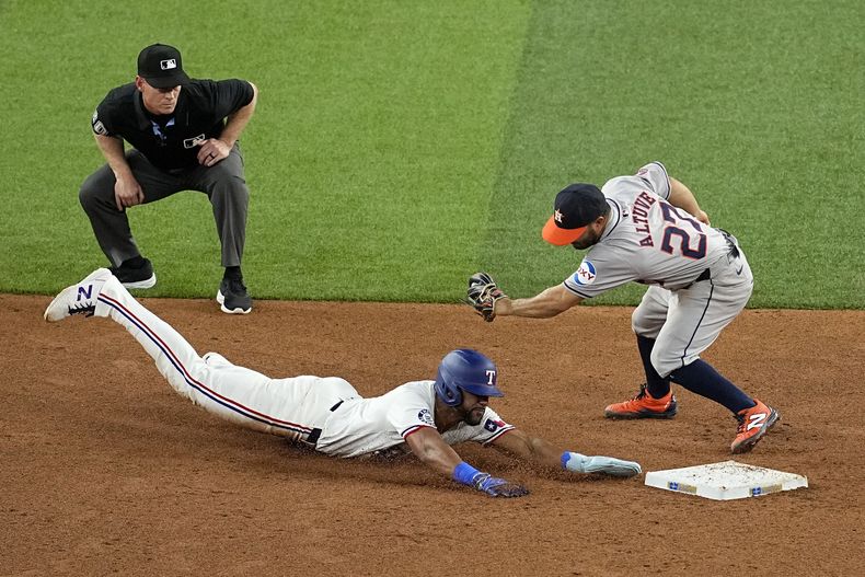 Leody Taveras de los Rangers de Texas se roba la segunda base evitando ser tocado por el venezolano de los Astros de Houston José Altuve, ante la mirada del árbitro Scott Barry durante la 6ta entrada del juego de béisbol en Arlington, Texas, el sábado 6 de abril de 2024. (AP Foto/Tony Gutierrez)