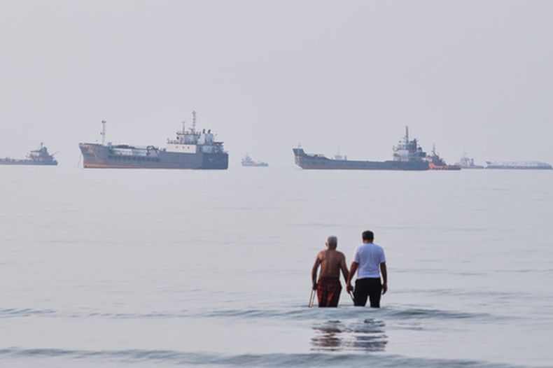 Dos hombres caminan en las aguas del estrecho de Ormuz con barcos fondeados más lejos, cerca de Bandar Abbas, Irán, el domingo 12 de julio de 2026. (Razieh Poudat/ISNA via AP)