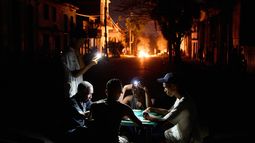 Varias personas se iluminan con sus teléfonos mientras juegan al dominó, al tiempo que arde en una calle de La Habana, Cuba, una hoguera provocada por los vecinos que protestaban contra los prolongados cortes de luz. (AP Foto/Ramón Espinosa)