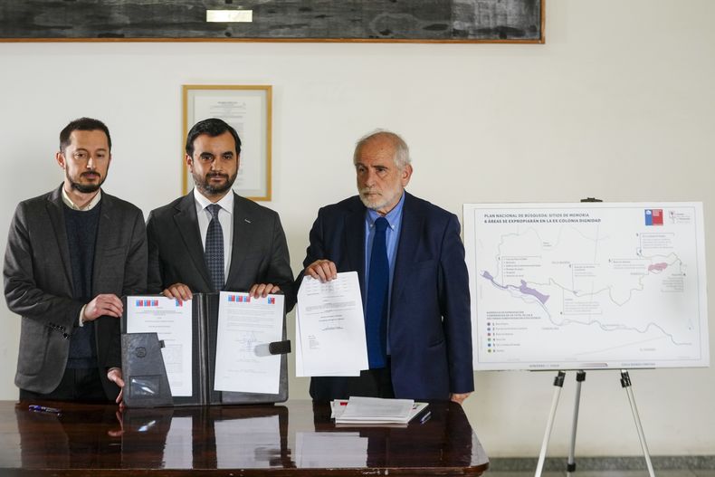 Los ministros chilenos, de izquierda a derecha: Francisco Figueroa, de Bienes Nacionales; Jaime Gajardo, de Justicia y Derechos Humanos; y Carlos Montes, de Vivienda y Urbanismo, sostienen un decreto firmado para que la antigua Colonia Dignidad, otrora centro de detención, tortura y exterminio durante la dictadura de Pinochet, se convierta en un espacio dedicado a la protección de los derechos humanos. Santiago de Chile, lunes 7 de julio de 2025. (Foto AP/Esteban Felix)