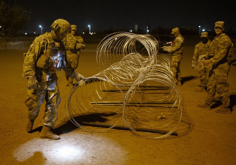 Elementos de la Guardia Nacional de Texas atan hileras de alambre de púas para su instalación cerca de una puerta en el muro fronterizo a primeras horas del jueves 11 de mayo de 2023, en El Paso, Texas. Gran cantidad de migrantes se apresuraban a cruzar la frontera horas antes de que el jueves expiraran las restricciones al asilo relacionadas con la pandemia de COVID-19, ante el temor de que las nuevas medidas les compliquen todavía más ingresar a Estados Unidos. (AP Foto/Andrés Leighton)