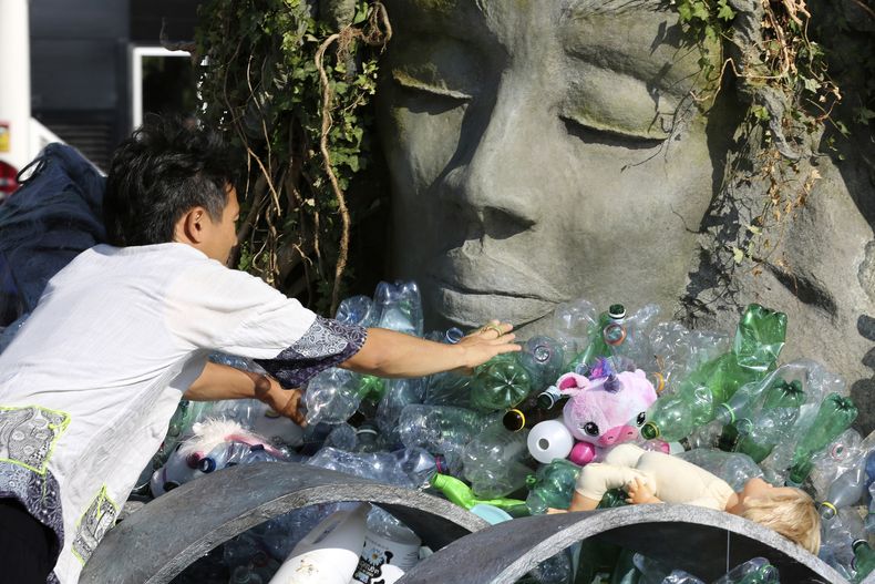 Benjamin Von Wong, a la derecha, un artista y activista canadiense, amontona pilas de desechos plásticos sobre una gran escultura que diseñó frente a la oficina de las Naciones Unidas en Ginebra, Suiza, el lunes 11 de agosto de 2025. (Foto AP/ Jennifer McDermott)