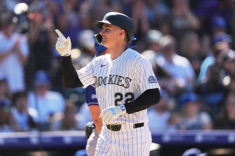 Mickey Moniak, de los Rockies de Colorado, al frente, hace un gesto al cruzar el plato después de conectar un jonrón de dos carreras ante el lanzador relevista de los Dodgers de Los Ángeles, Blake Treinen, en la séptima entrada de un juego de béisbol el domingo 19 de abril de 2026, en Denver. (AP Foto/David Zalubowski)