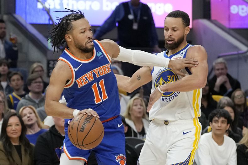 Jalen Brunson (11), de los Knicks de Nueva York, conduce el balón hacia la canasta con la marca de Stephen Curry, de los Warriors de Golden State, durante la primera mitad del juego de baloncesto de la NBA, en San Francisco, el lunes 18 de marzo de 2024. (AP Foto/Jeff Chiu)