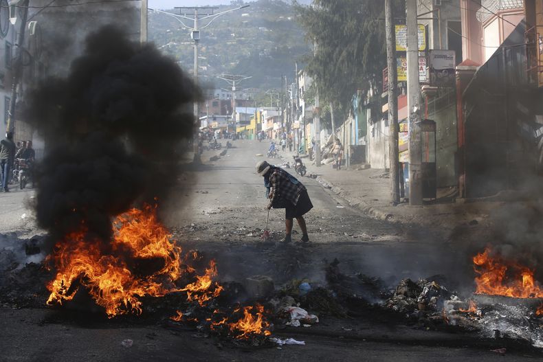 Una mujer barre cerca de los restos de una barricada en llamas colocada por manifestantes en una protesta contra la inseguridad en Puerto Príncipe, Haití, el miércoles 2 de abril de 2025. (AP Foto/Odelyn Joseph)