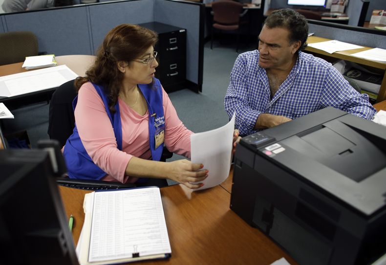 En esta foto del 6 de febrero de 2014, Rose Capote-Marcus, izquierda, ayuda a Waldemar Vega, de 50 a&ntilde;os, con tr&aacute;mites para recibir prestaciones por desempleo. El n&uacute;mero de personas que solicit&oacute; prestaciones aument&oacute; en 8.