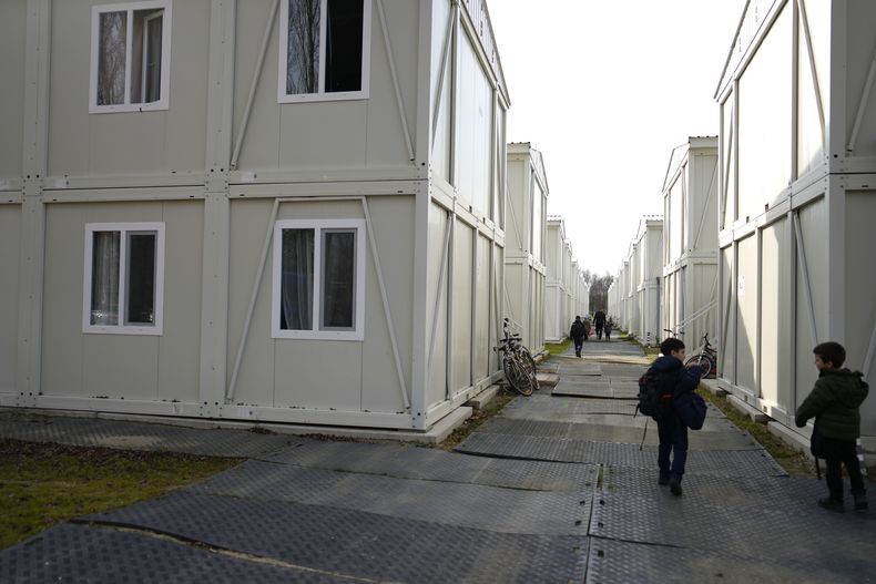 Niños que regresan de la escuela caminan entre apartamentos construidos con contenedores en un vecindario para familias ucranianas huidas de la guerra en Linkeroever, Bélgica, el viernes 17 de marzo de 2023. Pese a la cálida bienvenida que recibieron los millones de refugiados ucranianos en la Unión Europea tras la invasión rusa, las autoridades de la UE advirtieron el martes que hay temores a que el apoyo se reduzca por la influencia de la persistente propaganda rusa y una desaceleración económica que afecta especialmente a las familias pobres. (AP Foto/Virginia Mayo)