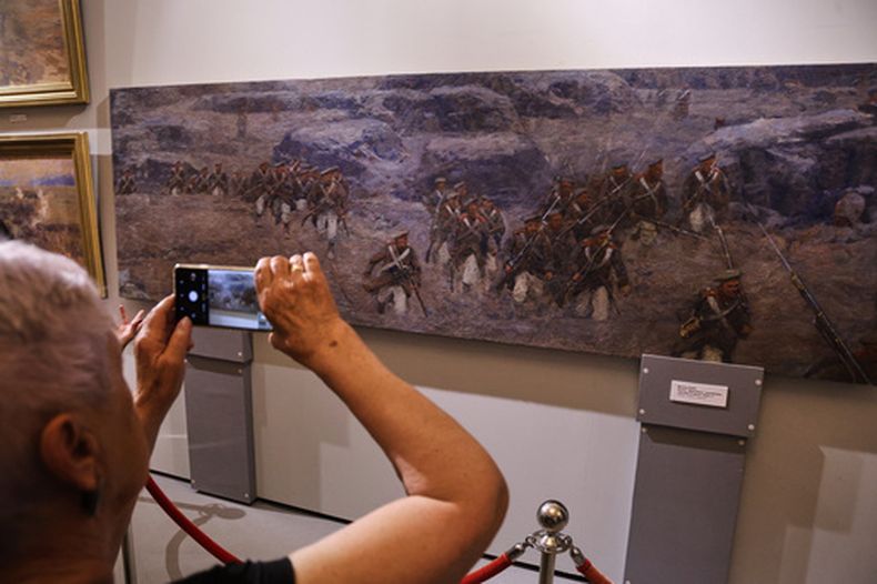 Una visitante toma una fotografía de una sección de un cuadro panorámico que representa la defensa de Sebastopol durante la guerra de Crimea del siglo XIX, la parte que se conservó aparte del panorama completo destruido por un ataque ucraniano, el jueves 11 de junio de 2026, en Sebastopol, Crimea. (Foto AP)