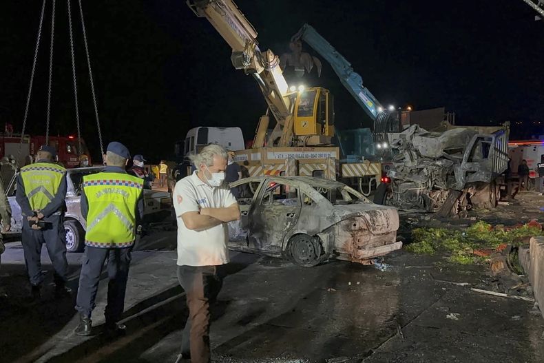 Agentes de policía y personal de emergencia trabajan junto a vehículos quemados tras un choque en la autopista entre Alejandreta y Antioquía, en el sur de Turquía, el sábado 6 de mayo de 2023. (IHA via AP)