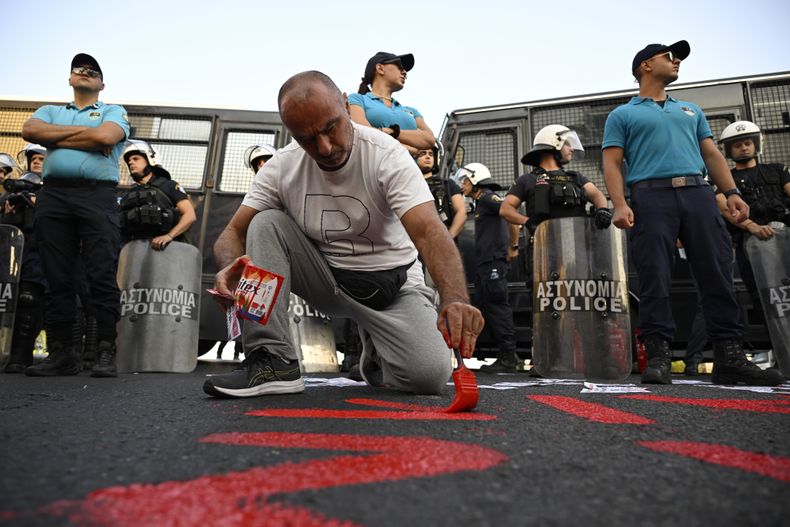 Un manifestante pinta una frase en el piso, frente a la policía, durante una protesta contra la llegada de un crucero con israelíes a bordo, en el puerto de Pireo, Grecia, el 14 de agosto de 2025. (AP Foto/Michael Varaklas)
