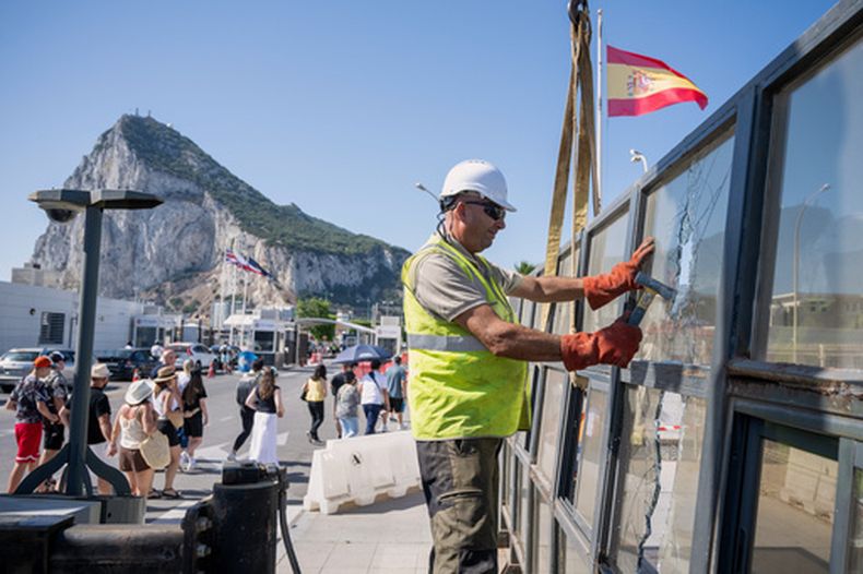 Con el Peñón de Gibraltar de fondo, varios trabajadores desmantelan un puesto de control fronterizo español que separaba de España el disputado territorio británico de ultramar en la Línea de la Concepción, España, el lunes 6 de julio de 2026. (AP Foto/Marcos Moreno)