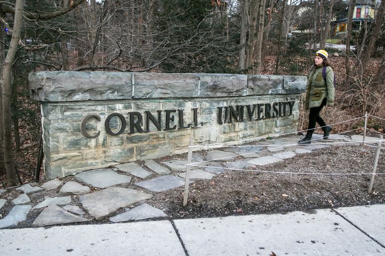 Una mujer camina junto a una placa de la Universidad de Cornell en el campus de la escuela de la Ivy League en Ithaca, Nueva York, el viernes 14 de enero de 2022. (AP foto/Ted Shaffrey, archivo)