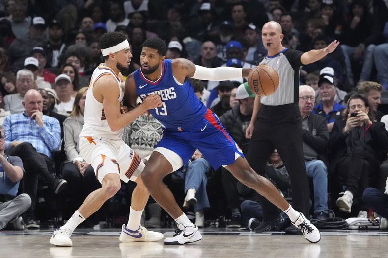 Paul George (centro), de los Clippers de Los Ángeles, trata de avanzar frente a Devin Booker, de los Suns de Phoenix, durante la primera mitad del juego de la NBA que ha enfrentado a ambos equipos, el 8 de enero de 2024, en Los Ángeles. (AP Foto/Mark J. Terrill)