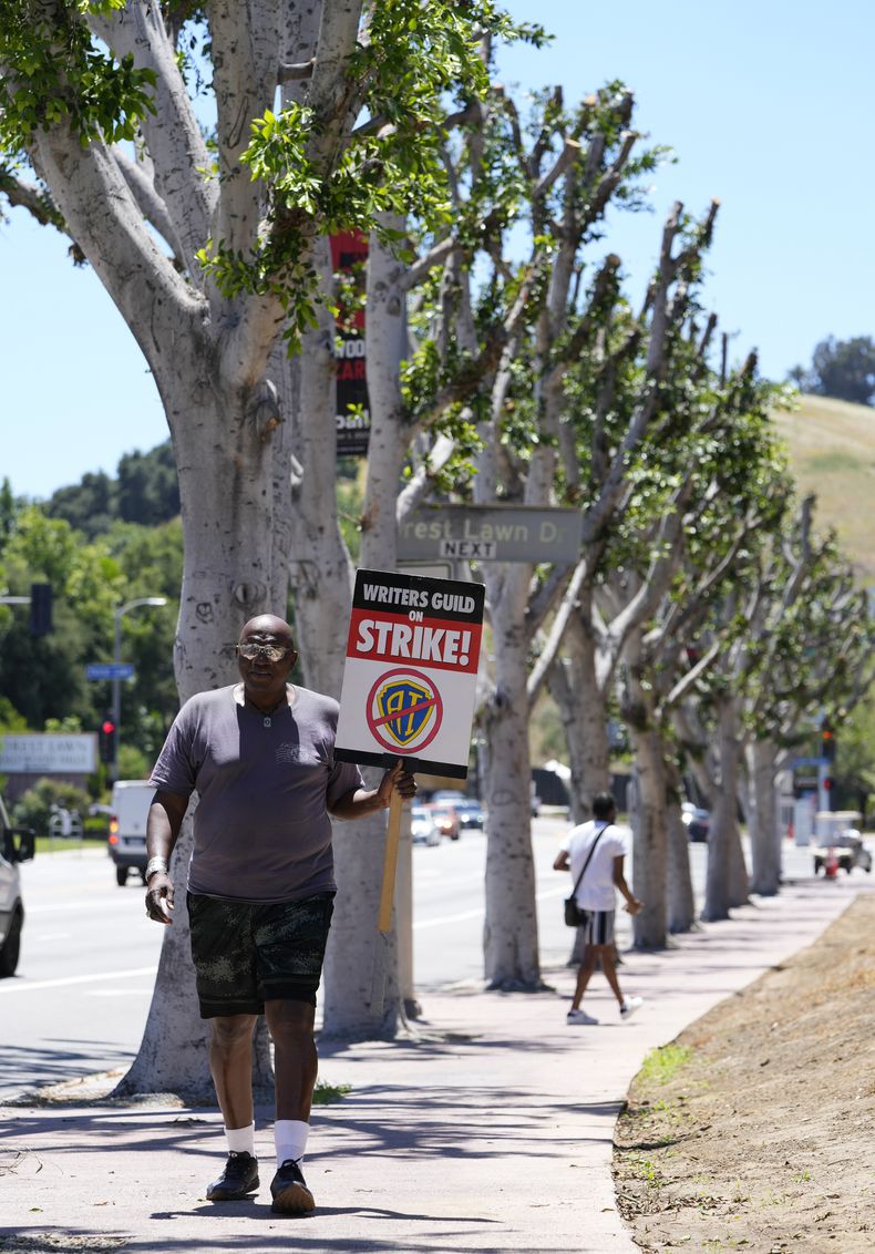 Dee Thompson, miembro del sindicato WGA y SAG-AFTRA, pasa junto a unos árboles árboles recién podados con un cartel en una manifestación frente a los estudios Universal el miércoles 19 de julio de 2023 en Burbank, California. (Foto AP/Chris Pizzello)