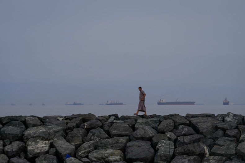 ARCHIVO - Un hombre camina por la orilla del mar mientras buques petroleros y de carga se alinean en el estrecho de Ormuz, vistos desde Khor Fakkan, Emiratos Árabes Unidos, el miércoles 11 de marzo de 2026. (AP Foto/Altaf Qadri/Archivo)