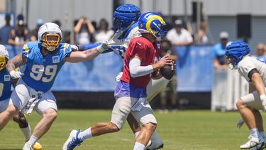Matthew Stafford, de rojo, quarterback de los Rams de Los Ángeles, corre con el balón durente una práctica conjunta ante los Chargers de Los Ángeles, en The Bolt, en El Segundo, California, el domingo 4 de agosto de 2024. El tackle defensivo de los Chargers Scott Matlock (99) busca presionar a Stafford. (AP Foto/Damian Dovarganes)