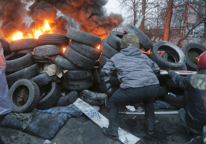 Actistas tratan de localizar a un francotirador resguard&aacute;ndose en una barricada hecha con llantas viejas cerna de la plaza Independencia de Kiev, capital de Ucrania el jueves 20 de febrero de 2014. (Foto de AP/Efrem Lukatsky)