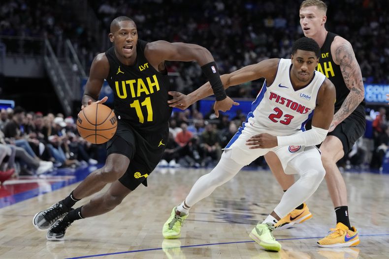 Kris Dunn, del Jazz de Utah, avanza junto a Jaden Ivey, base de los Pistons de Detroit, en el encuentro del jueves 21 de diciembre de 2023 (AP Foto/Carlos Osorio)