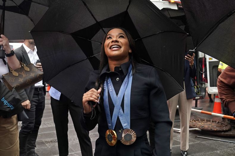 Jordan Chiles, dos veces medallista olímpica de gimnasia estadounidense, mira bajo una sombrilla un video de ella misma afuera del Nasdaq MarketSite, luego de tocar la campana de cierre, en Times Square, Nueva York, el jueves 8 de agosto de 2024. (Foto AP/Richard Drew)