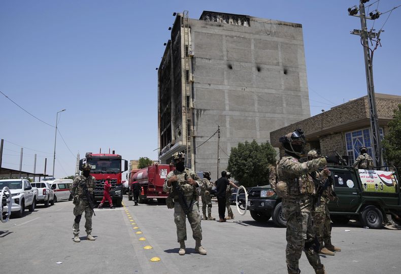 Fuerzas de seguridad iraquíes se reúnen ante el edificio de un centro comercial incendiado en Kut, Irak, el jueves 17 de julio de 2025. (AP Foto/Hadi Mizban)